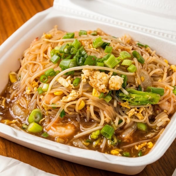 Styrofoam takeout container filled with shrimp lo mein, garnished with green onions and broccoli.