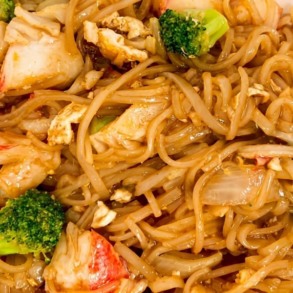 Close-up of crab pad see ew with flat noodles, broccoli, and onions in a white takeout container.
