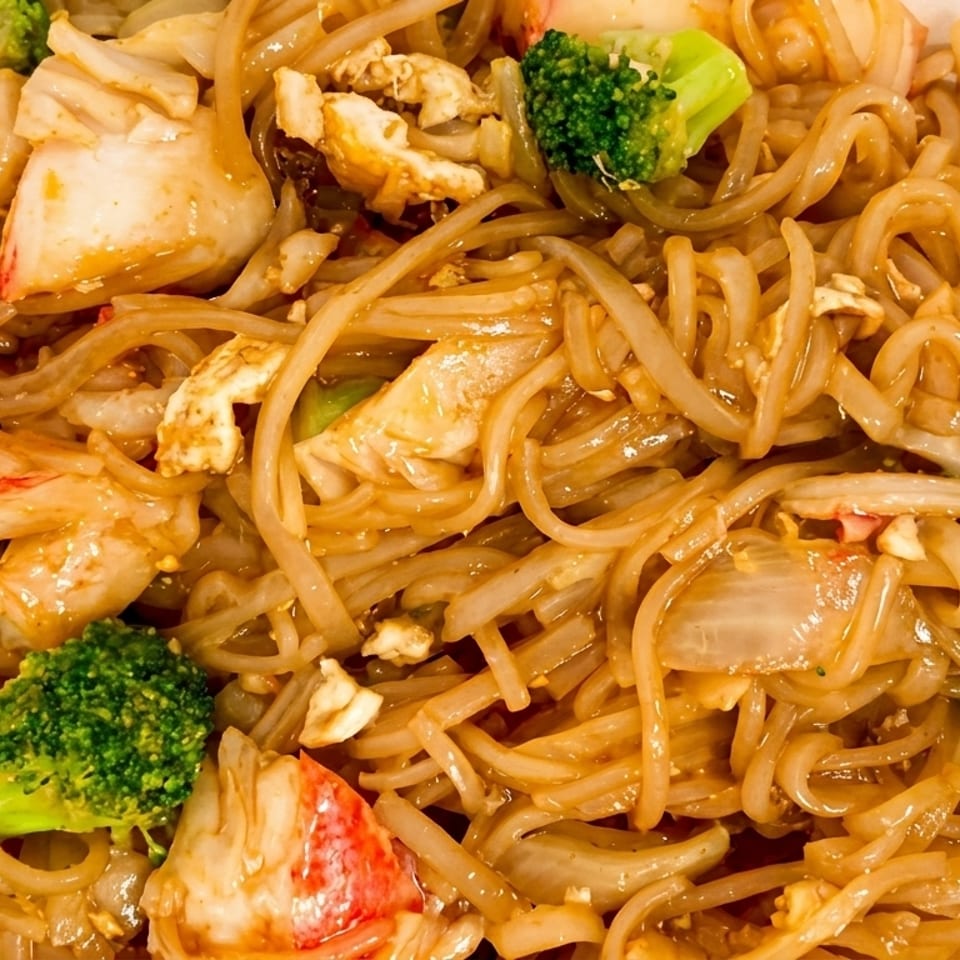 Close-up of crab pad see ew with flat noodles, broccoli, and onions in a white takeout container.